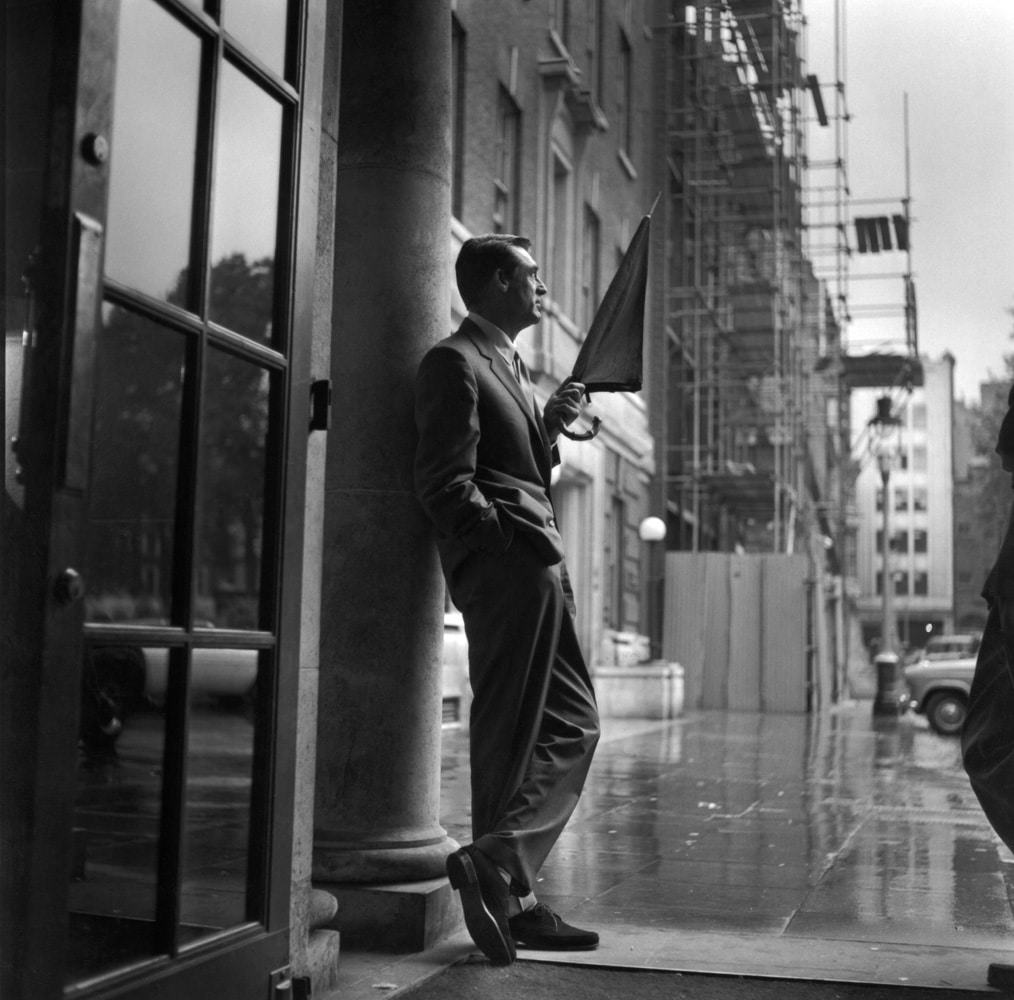 British-born American actor Cary Grant (1904 - 1986) sheltering in a hotel porch as he waits for the rain to stop.  (Photo by Express/Getty Images)